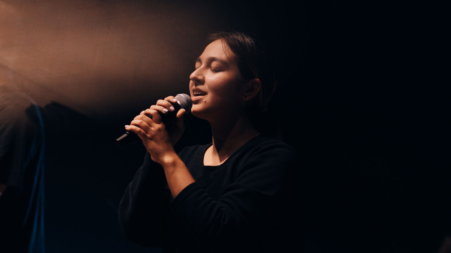 Une chanteuse au micro, sur scène dans la pénombre