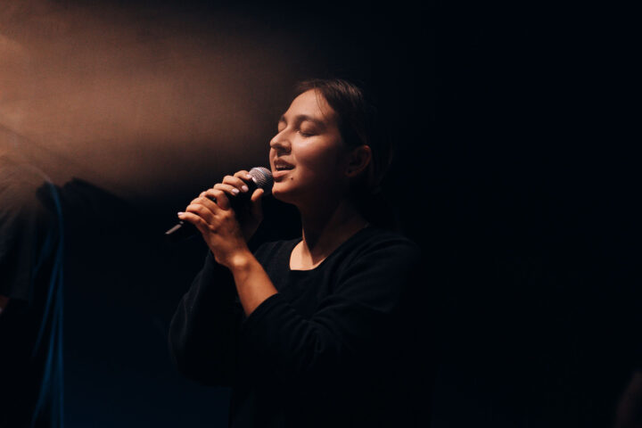 Une chanteuse au micro, sur scène dans la pénombre