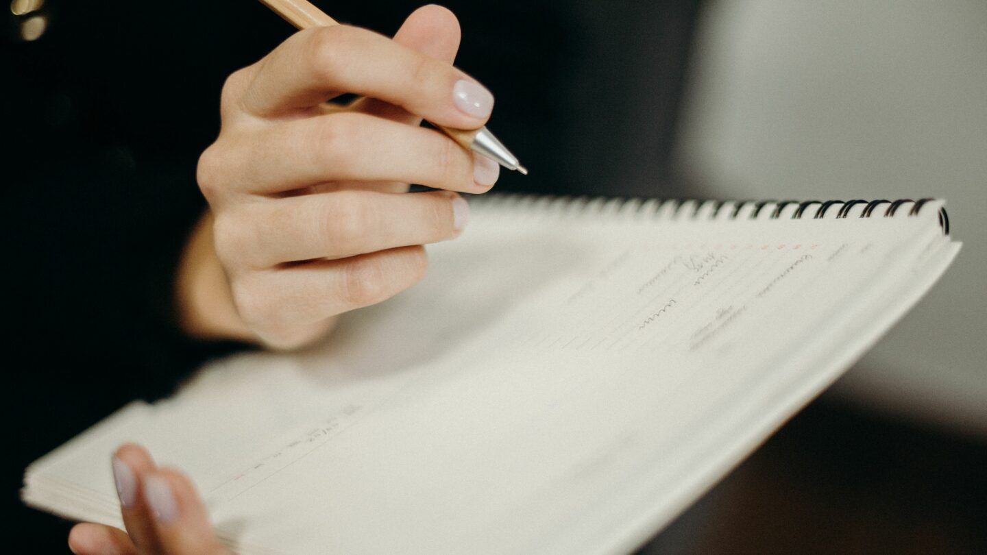 Une main prend des notes au stylo dans un carnet