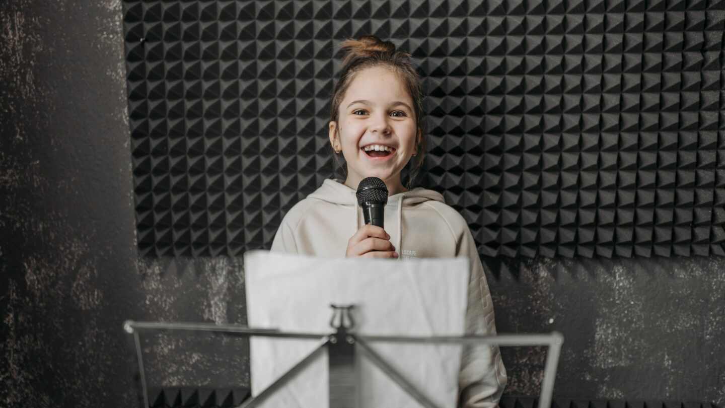 Une jeune fille sourit en chantant au micro dans un studio, devant un pupitre