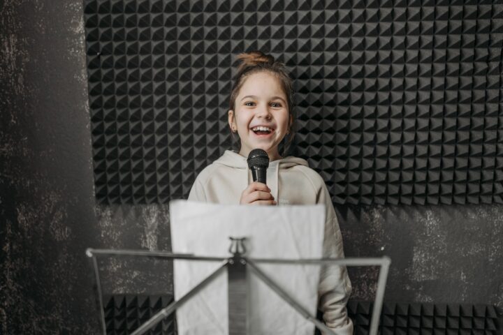 Une jeune fille sourit en chantant au micro dans un studio, devant un pupitre