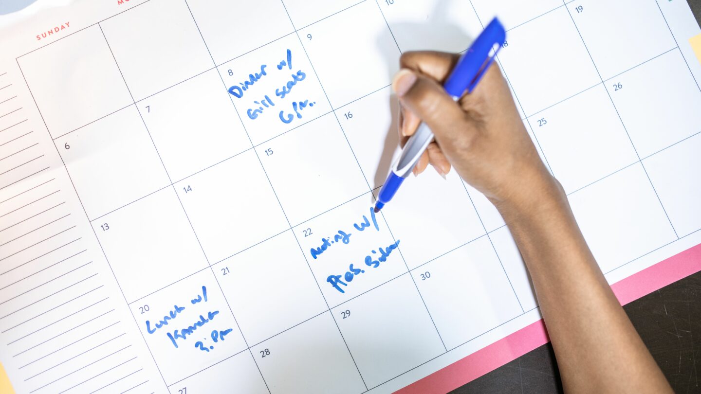 Une main note des rendez-vous au feutre bleu sur un calendrier mensuel
