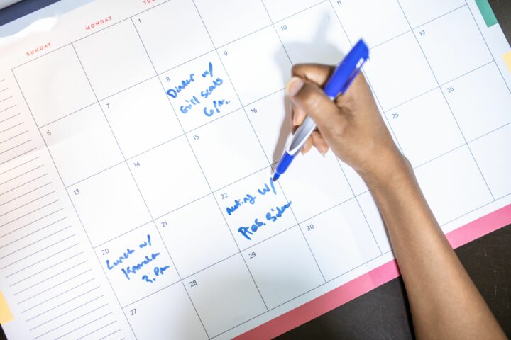 Une main note des rendez-vous au feutre bleu sur un calendrier mensuel